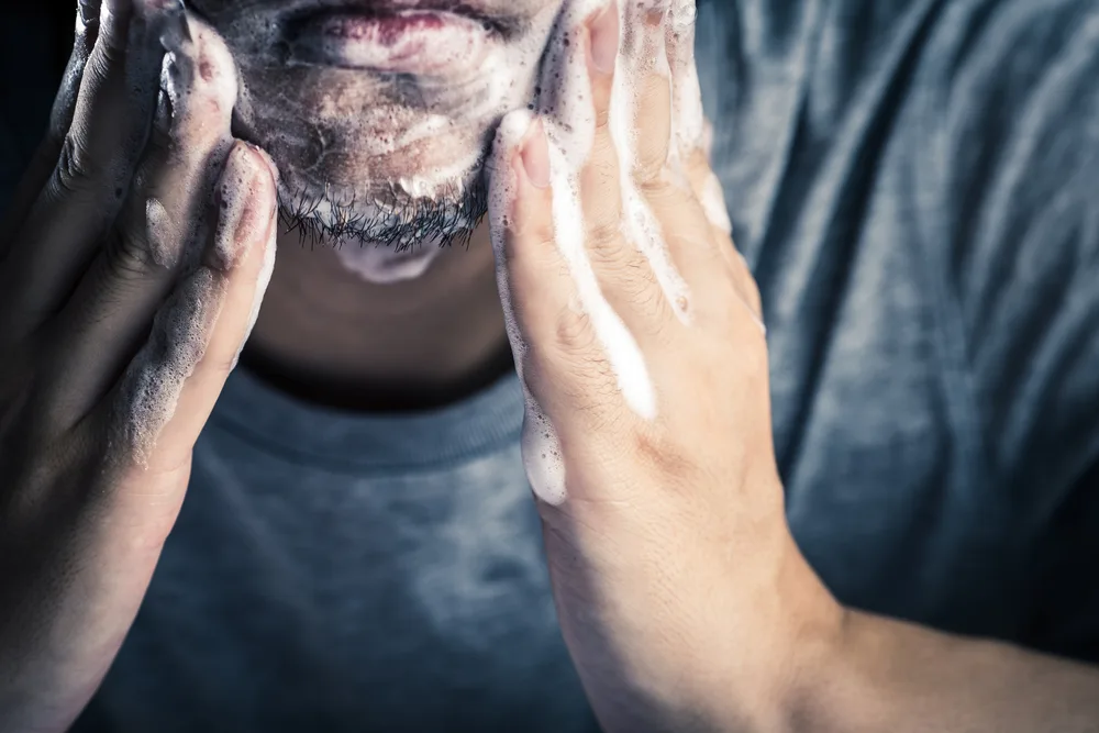 Man washing his beard for a piece on how to grow a beard featuring a man in a grey shirt with beard wash