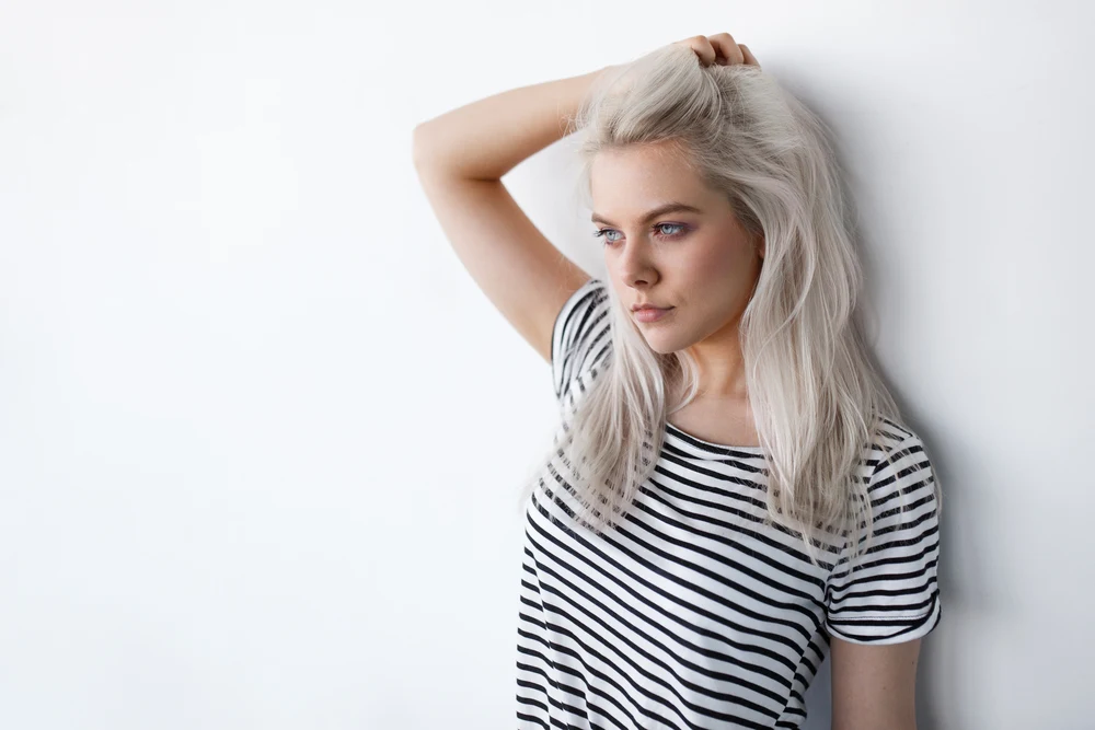 Woman wondering how to make grey hair shiny silver and holding her head