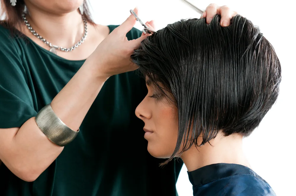 Woman getting a short haircut for thick hair in a salon while closing her eyes