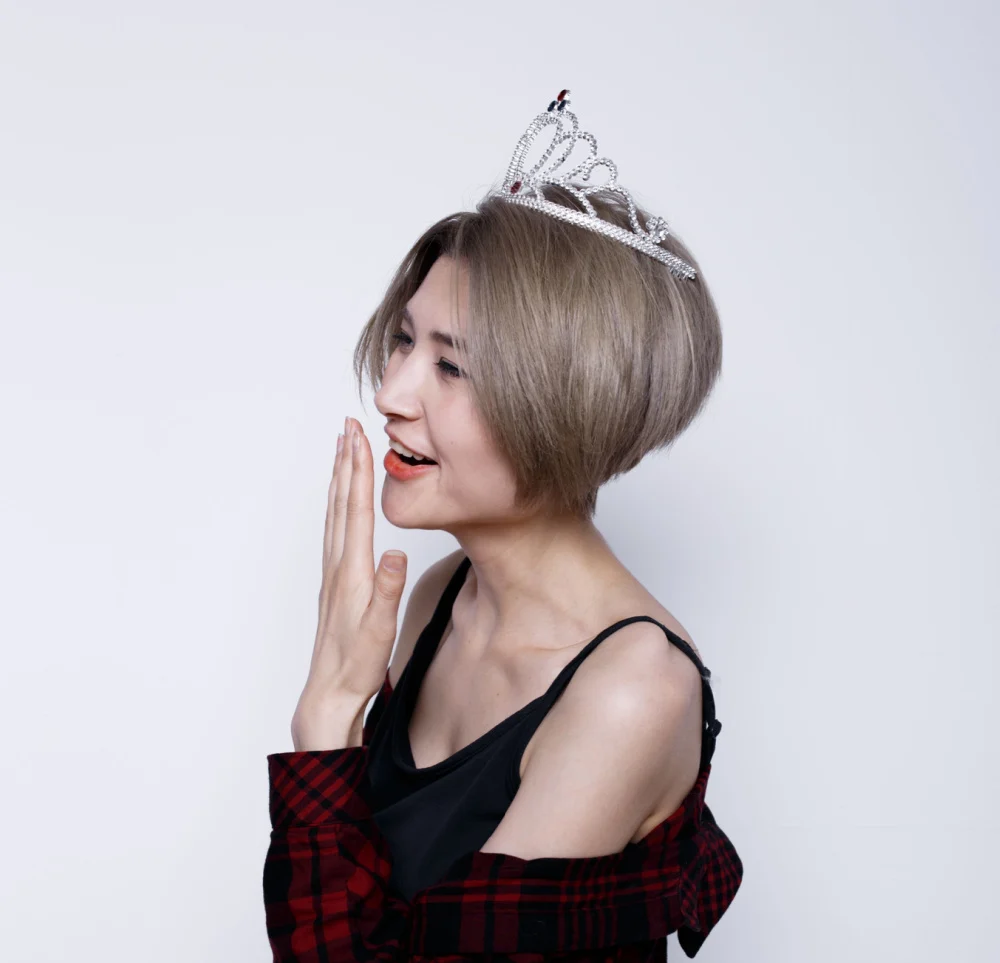 Woman wearing crown covers mouth and smiles after winning best hair color for short hair