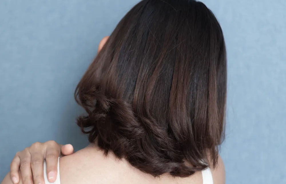 Back view of woman with hand on her shoulder showing off a long bob with curled ends and dark brown color