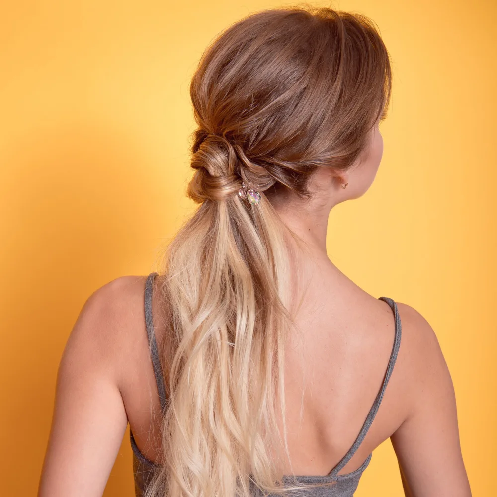 Back view of woman standing in front of orange wall with ombre hair in a cute hairstyle for long hair, a low twisted ponytail