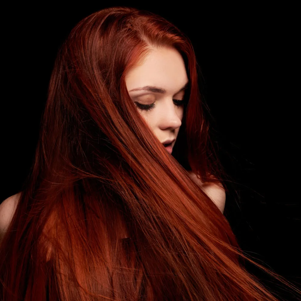 Woman in darkness with long straight blood orange color showing off one of the best warm red hair colors