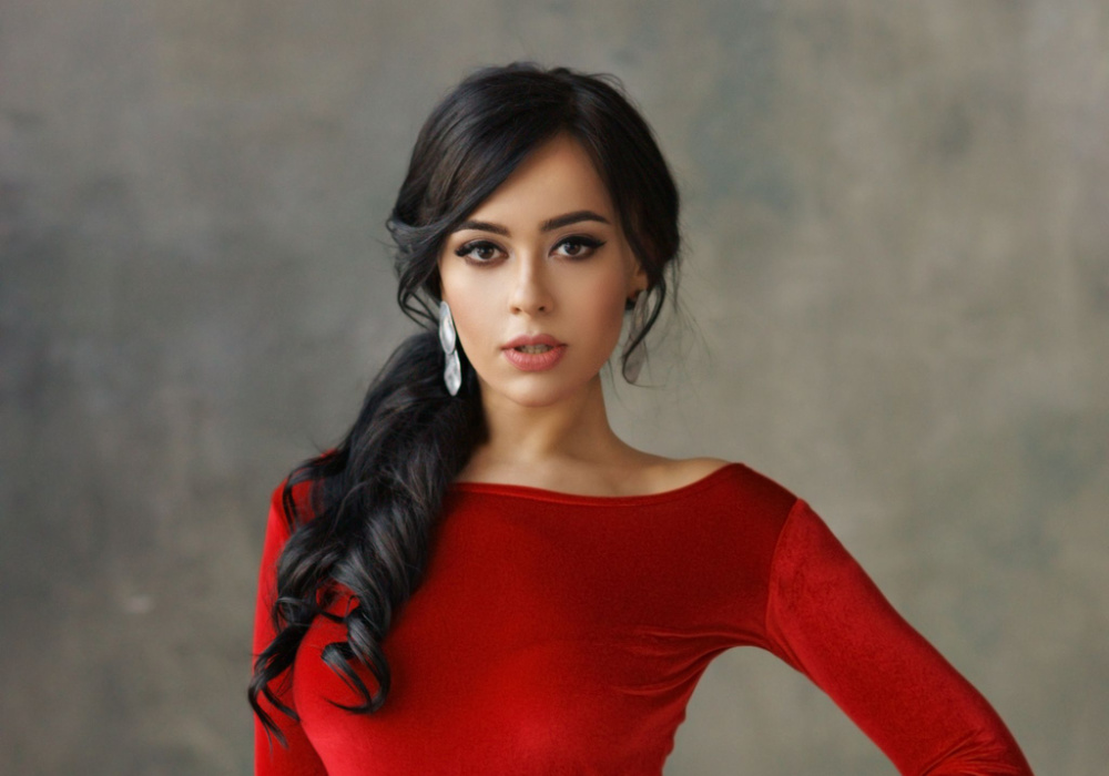 Dark-haired woman in vibrant red long-sleeved dress wears one of the hairstyles for long thin hair with a curly low ponytail and side part