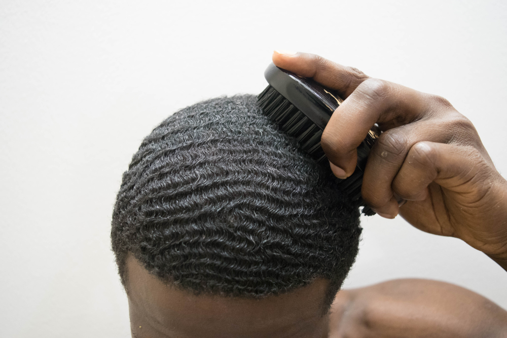 Black man brushing his hair with a boar bristle brush and using the best products for waves in a studio