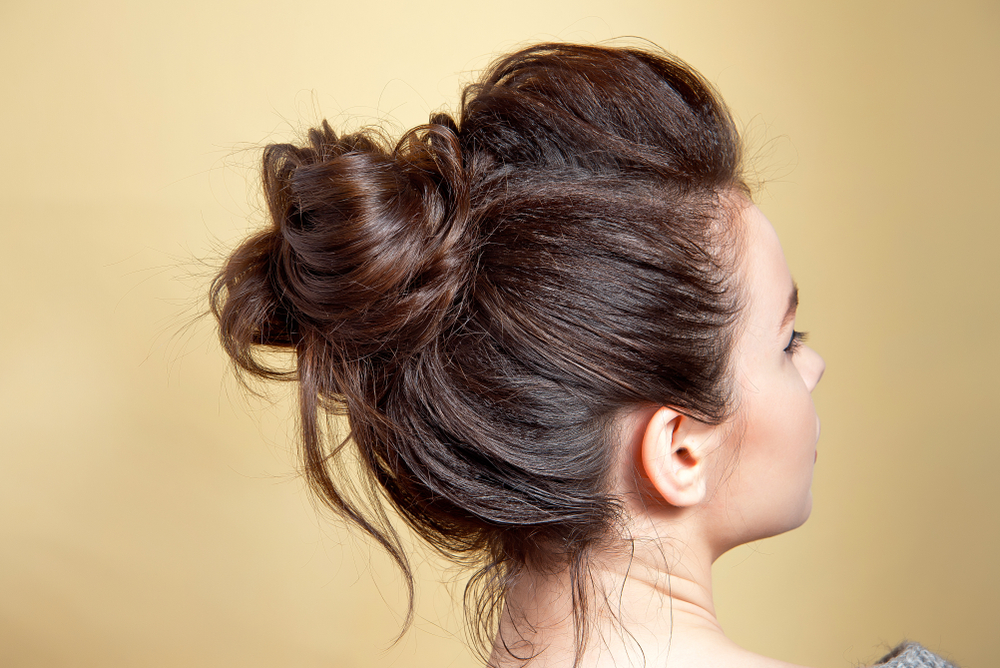 Back view of woman in front of yellow wall wearing her thin long hair in a messy bun hairstyle with extra volume in front