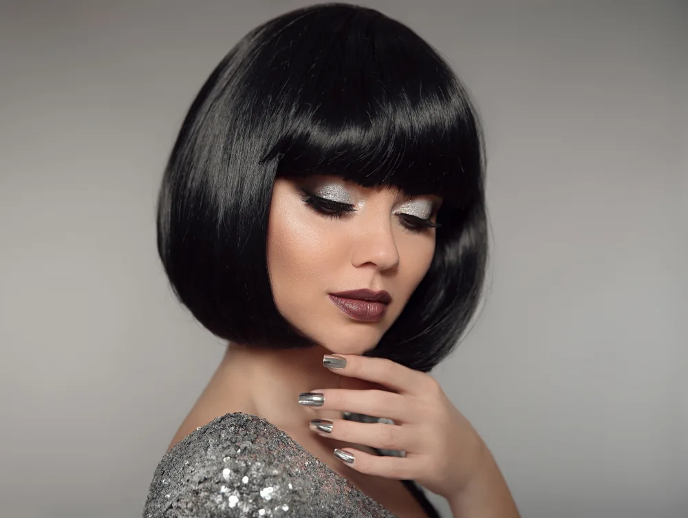 Woman touches chin with silver makeup and black hair to show off the best hair color for short hair in evening gown