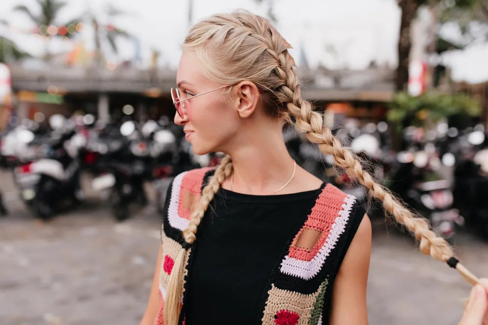 Woman in patterned sleeveless knit cardigan shows one of her favorite hairstyles for thin hair with twin French braids