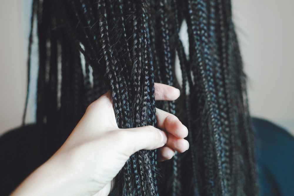 Woman grabs handful of small box braids to show their texture close up