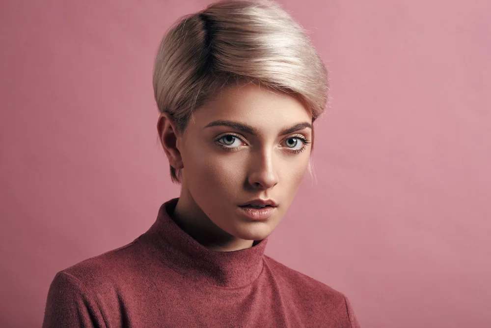 Woman with mouth open in front of pink wall looks straight with platinum as one of the top hair colors for short hair