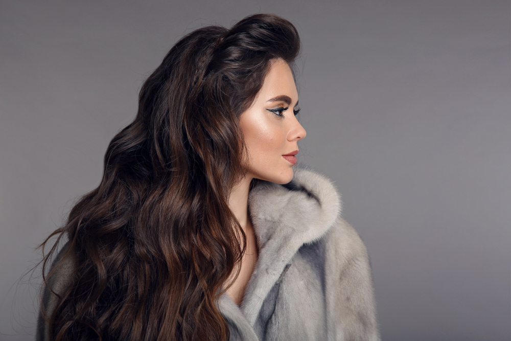 Dark haired woman glances away with fur coat and shows off voluminous waves with braided headband for long hair