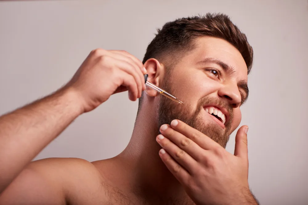 Guy using the best beard oil on his face while holding his left hand to his chin