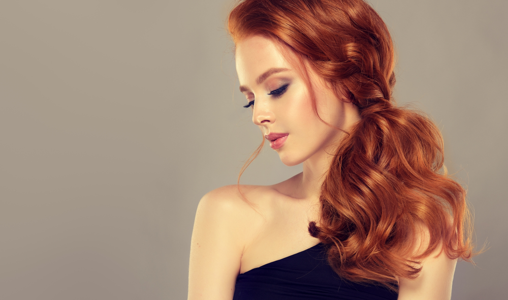Woman looks down with copper red hair on beige background to show the best hair color for dirty blondes