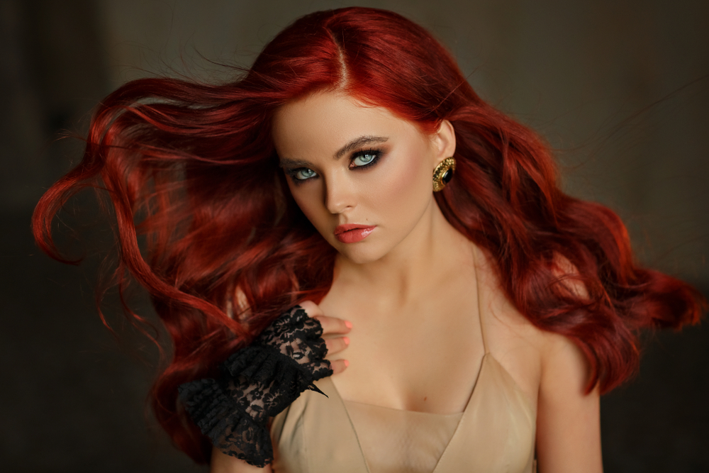 Woman with sultry stare wears a nude dress with black lace gloves and sports crimson as one of the best warm red hair colors