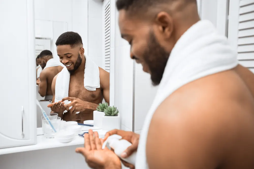 Man putting one of the best hair products for waves into his hand and smiling in a bathroom mirror