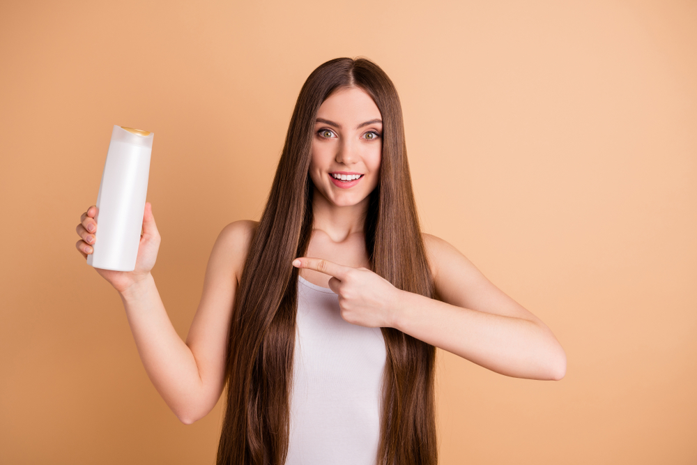 Woman holding a bottle of the best color-depositing shampoo and pointing at the bottle