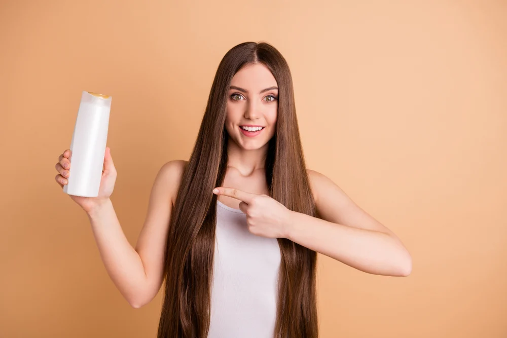 Woman holding a bottle of the best color-depositing shampoo and pointing at the bottle
