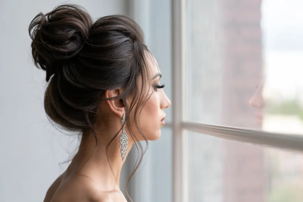Woman stares out the window with formal example of hairstyles for long thin hair in a voluminous bun with sparkly earrings dangling