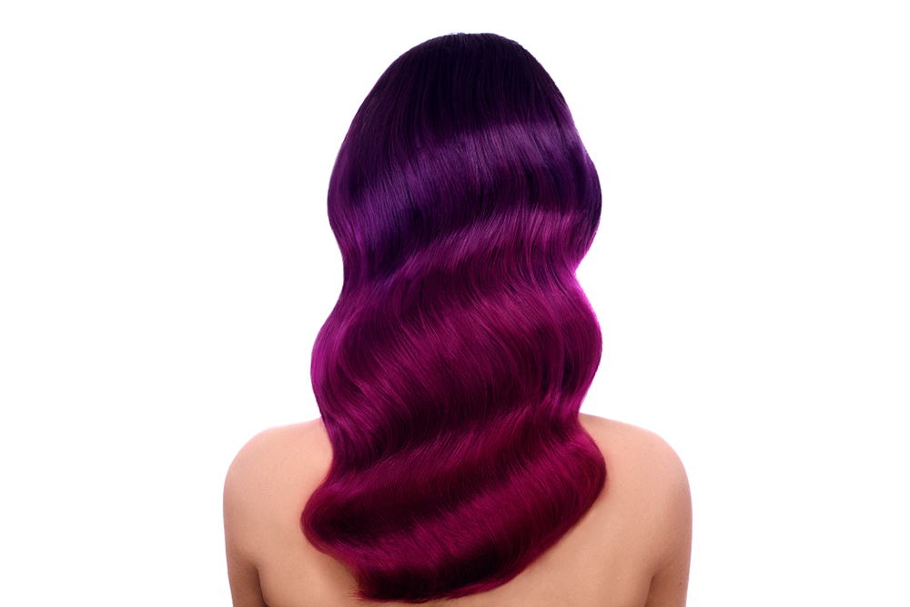 Back view of woman with long wavy dark violet and pink ombre hair in front of white background