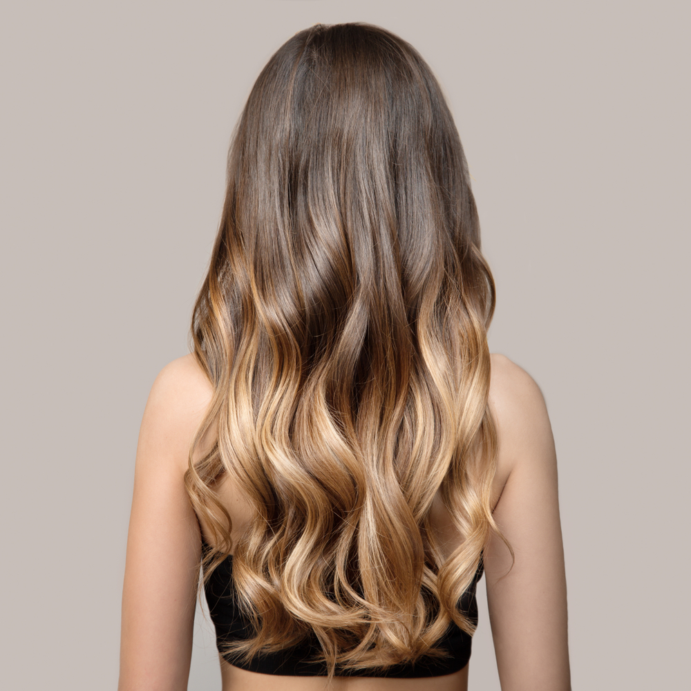 Back view of woman with long hair styled in loose waves with brown to blonde ombre color