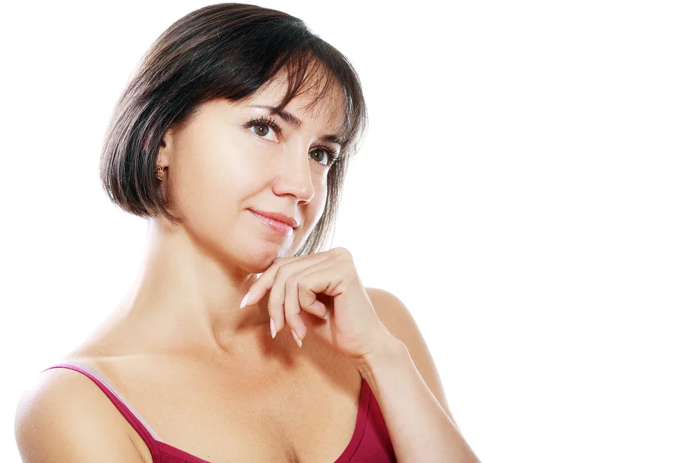Thoughtful brown haired woman with hand under chin wears a red tank top with a short bob and wispy bangs