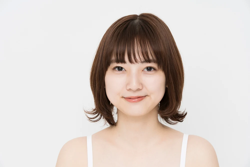 Young Japanese woman in a white tank top sports a bob with curled-up ends and textured wispy bangs across the forehead
