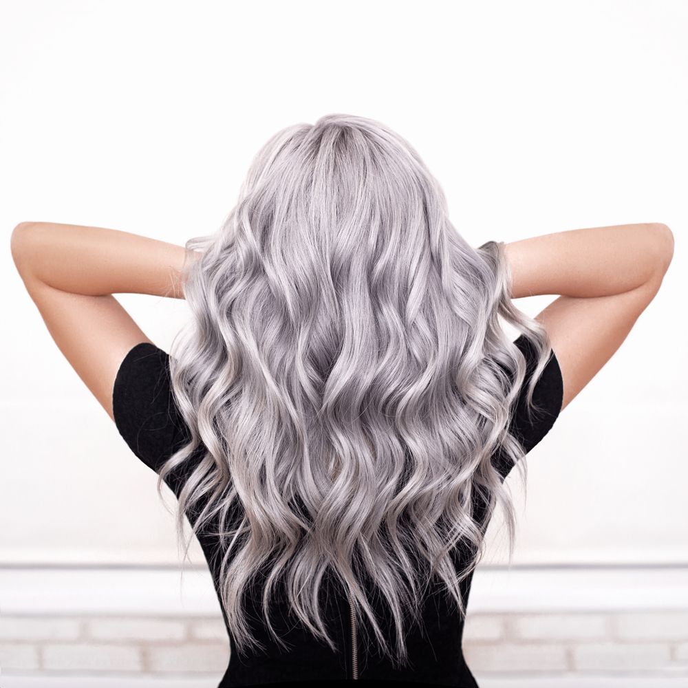 Woman with long silver hair has her hands raised to lift her medium beach waves hair style with tousled texture