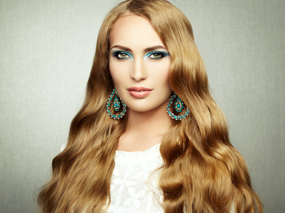 Woman with a small smile and turquoise earrings looks ahead with wavy honey blonde hair and copper undertones