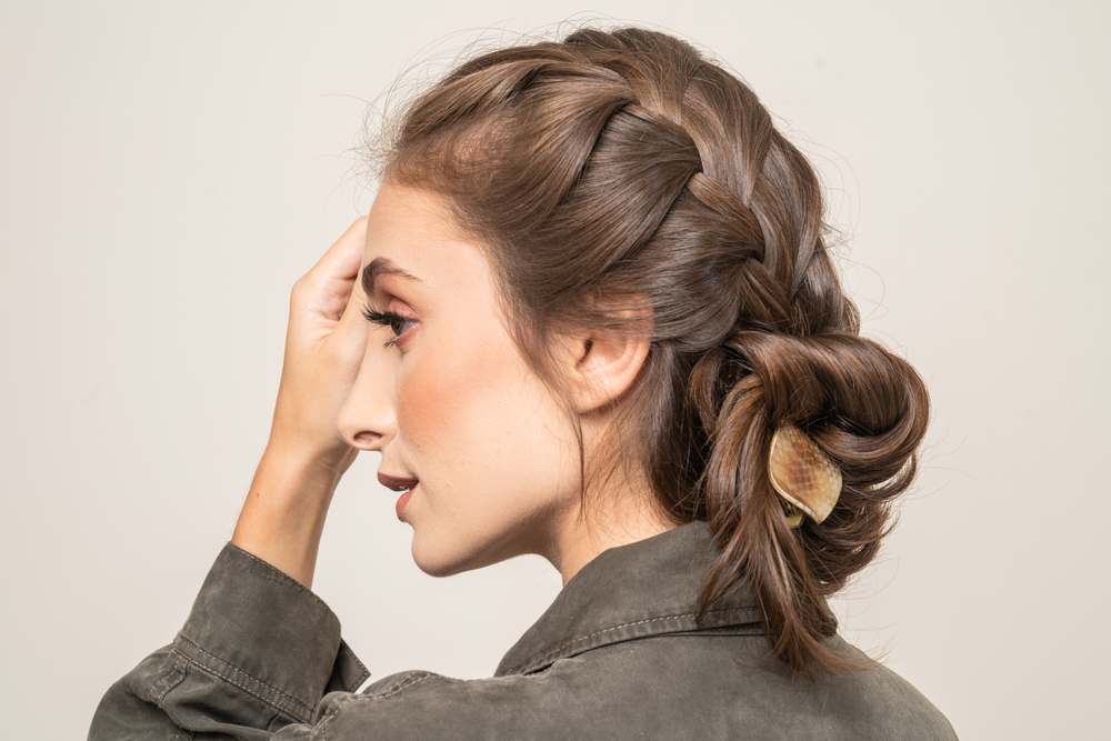 Back side view of woman in green jacket turning her head and touching face with one of many hairstyles for long thin hair featuring French braids and buns