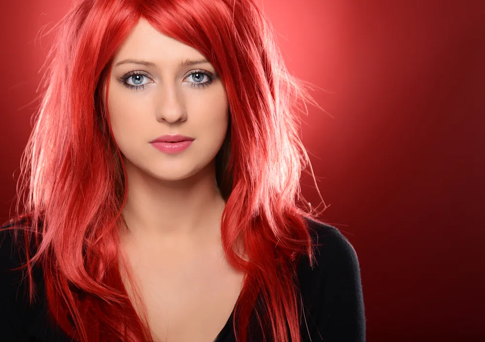 For a roundup of the best hair colors for red hair, a woman wears Watermelon Red hair and a black shirt