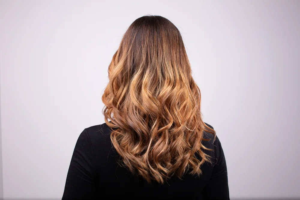 Back view of woman with long curly hair in a honey blonde color done with the balayage technique