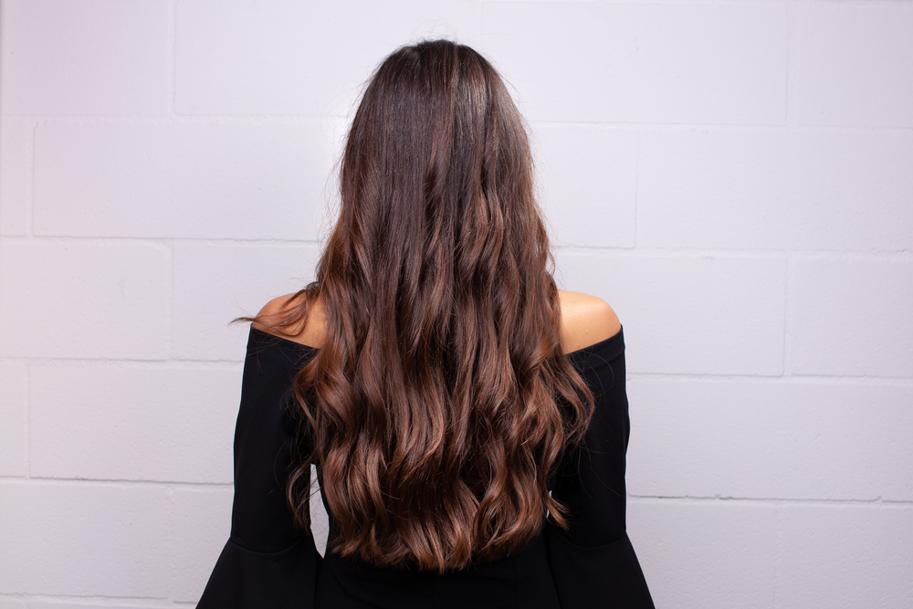 Rear view of woman wearing an off-shoulder black top with long hair featuring dark brown and auburn balayage