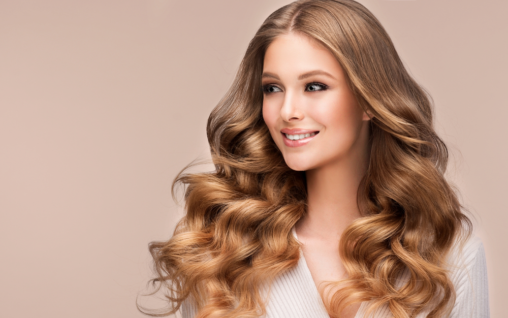 Woman glances away smiling with voluminous curls and honey blonde hair color 