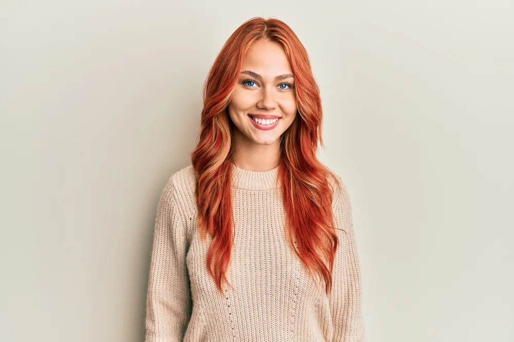 Smiling woman in sweater with soft coral hair has one of the most beautiful warm red hair colors