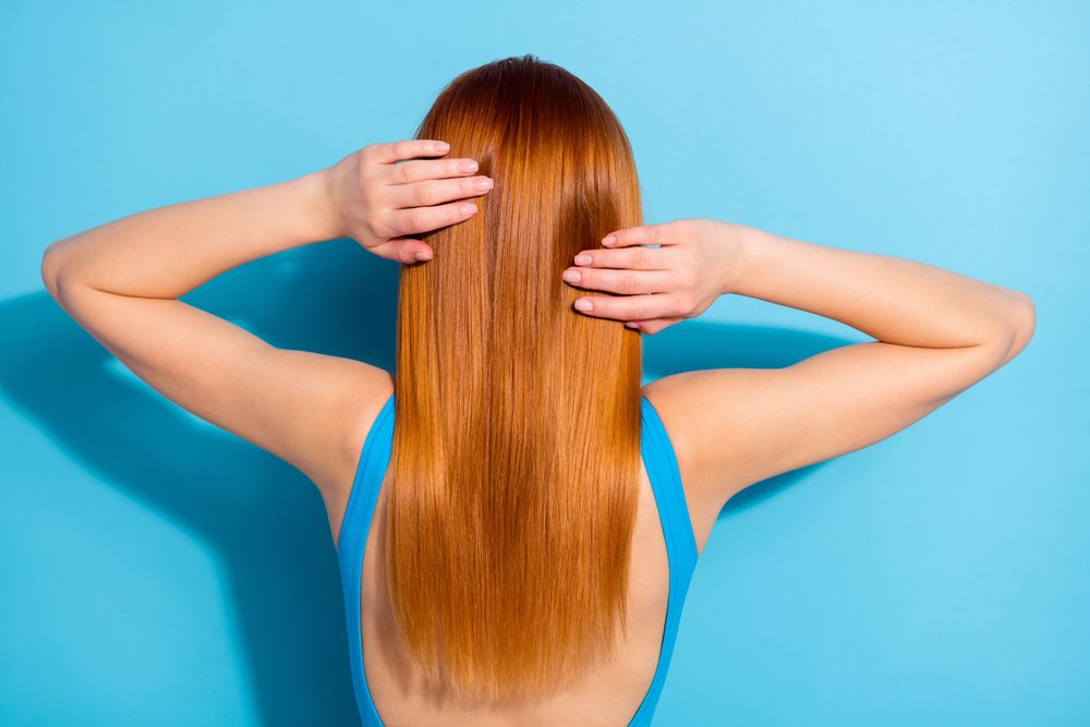 Light copper, one of the best hair colors for red hair on a woman in a blue shirt standing in a blue room