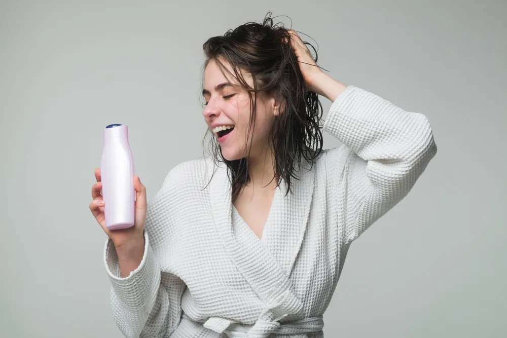 Woman in a white bath robe holding the best curl enhancers for wavy hair along with her hair