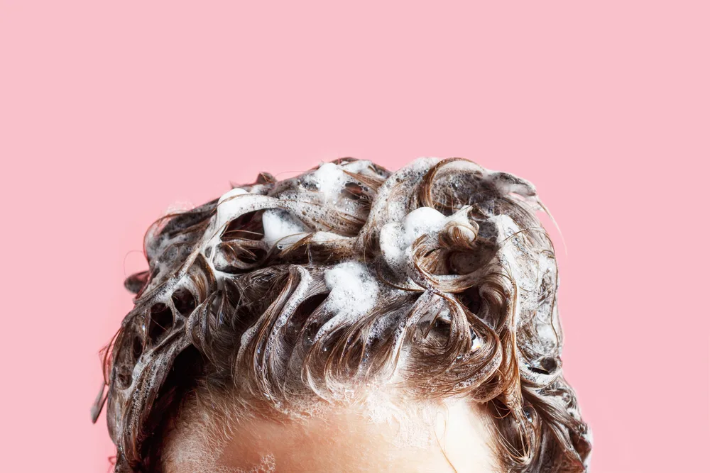 Woman using the best shampoo for dark colored hair on her hair with soapy suds sticking up from her hair