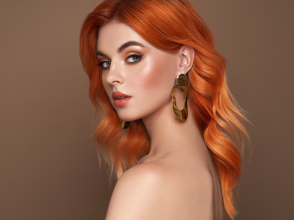 Woman with bare shoulders and orange copper hair color shows off medium beach waves hair style in a loose half-bend look
