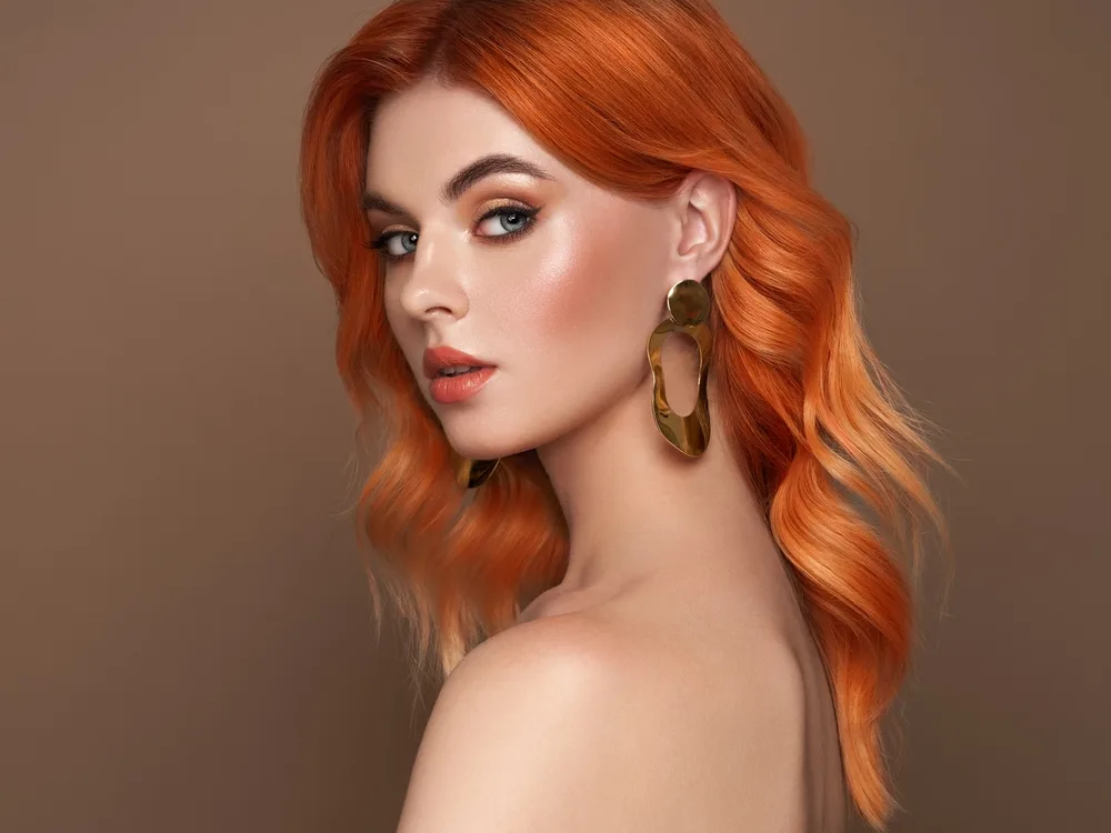 Woman with bare shoulders and orange copper hair color shows off medium beach waves hair style in a loose half-bend look
