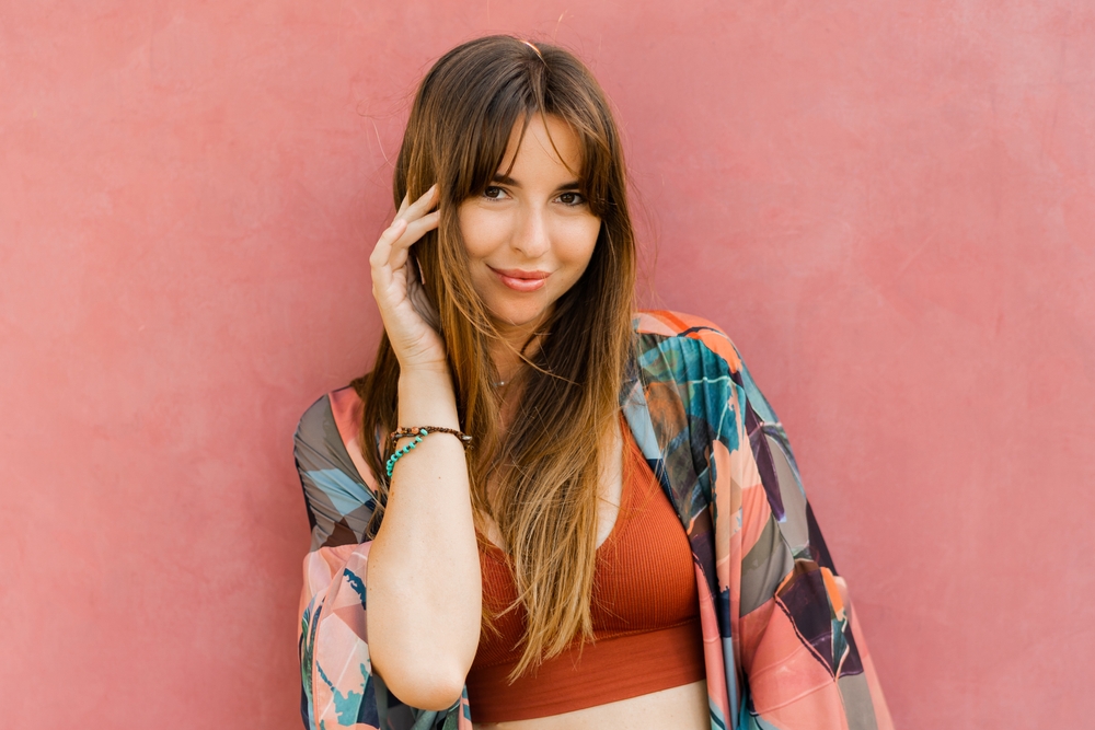 Smiling woman touches her face with patterned cardigan and crop top while wearing cute French bangs hairstyle with long hair
