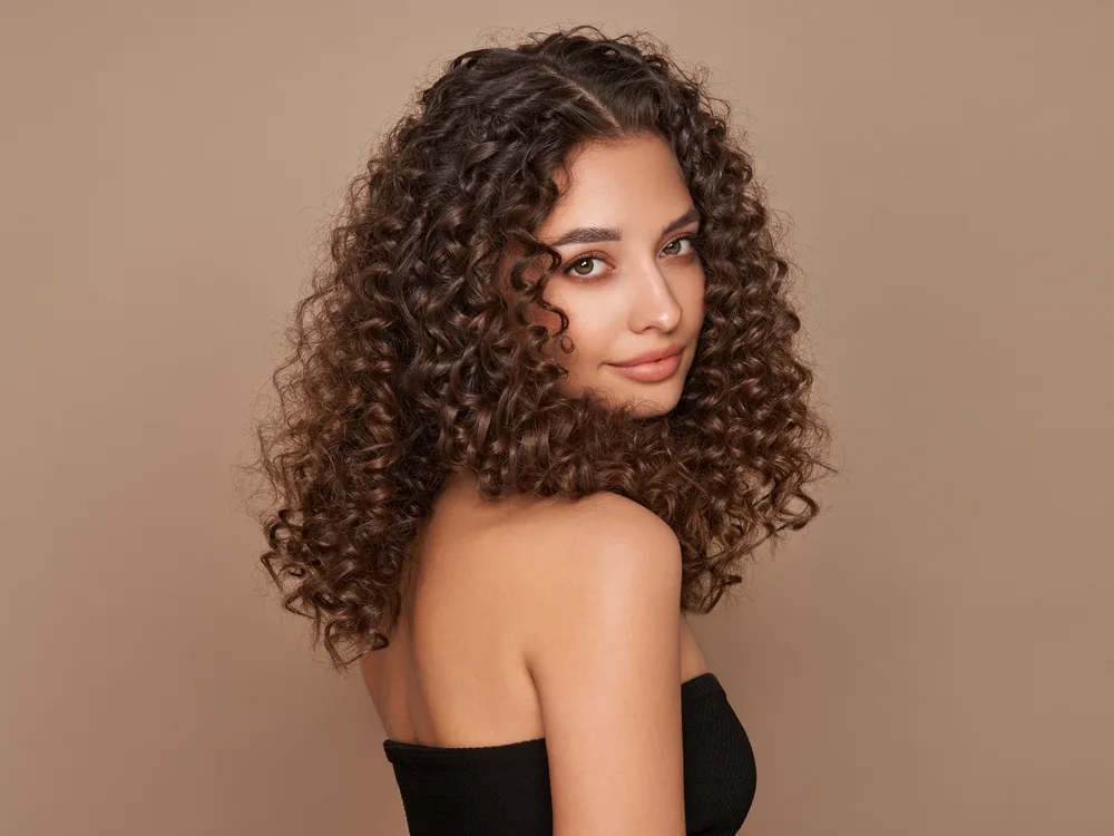 Woman in a studio rocking the best hair color for curly hair, brown