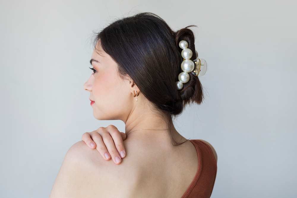 Brunette woman wearing one-shoulder red dress shows off one of the easy hairstyles for long thin hair with a quick claw clip updo