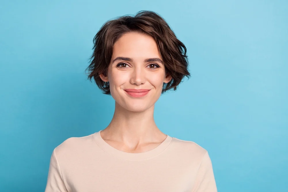 Smiling woman with dark brown wavy short hair stands in front of a blue background