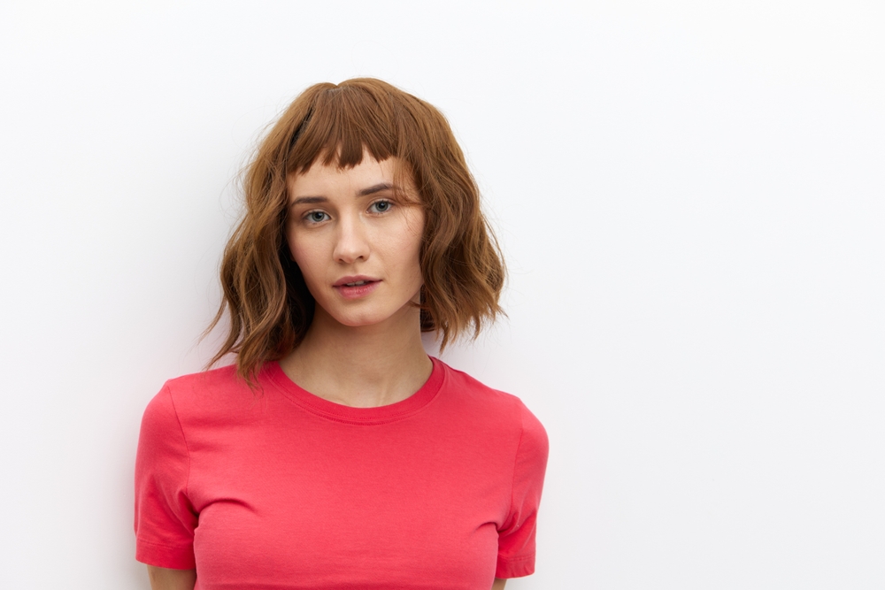 Woman stands against white wall with pink shirt wearing cinnamon as one of the best hair color for short hair