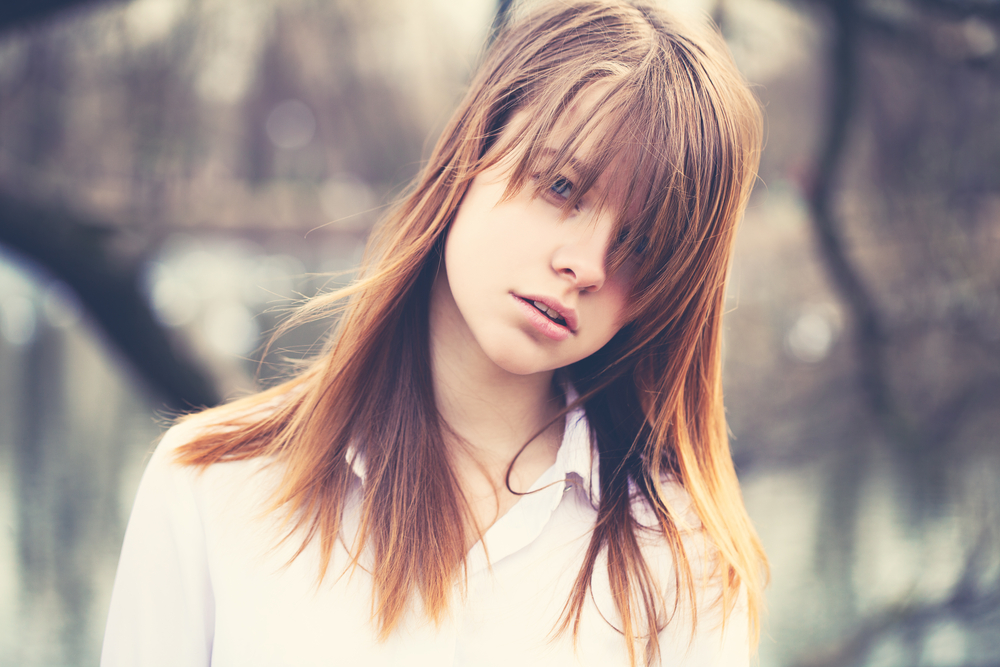 Girl with light brown hair and white collared shirt has medium-long hair with angled bangs