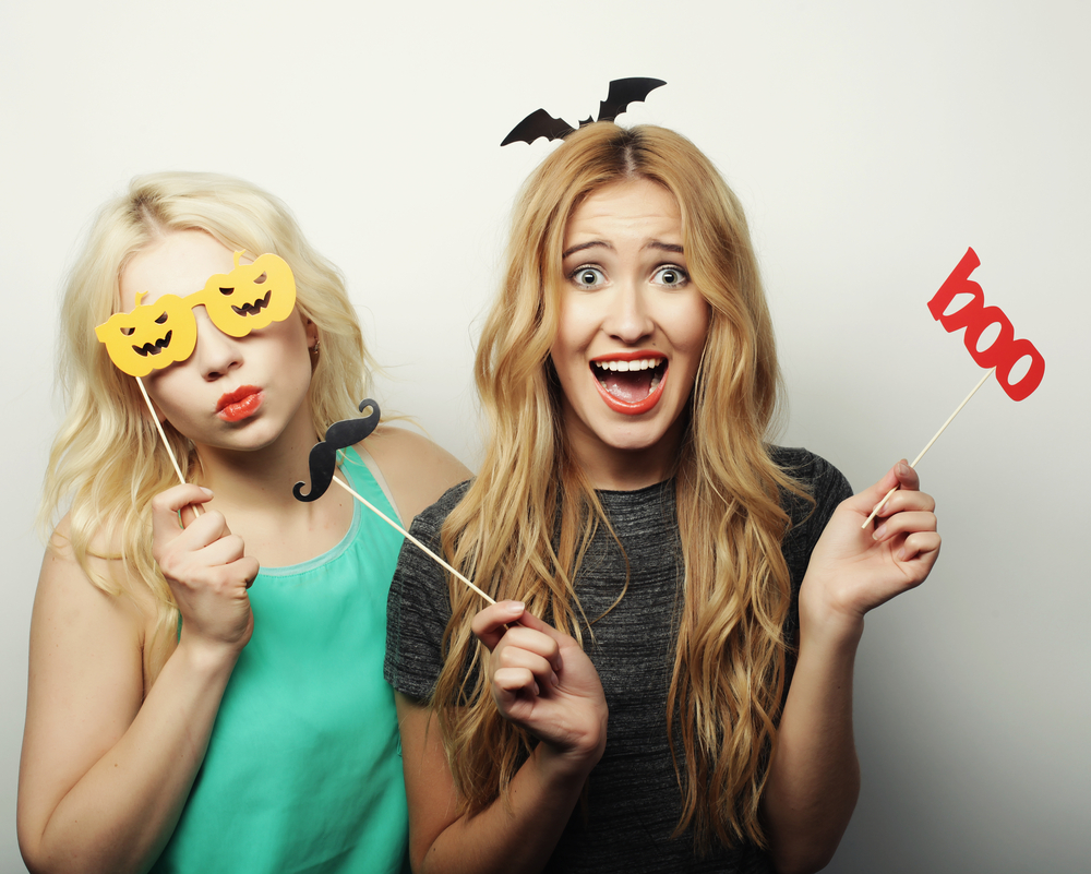 Two blonde woman show off their ideas for the best Halloween costumes for blondes while dressing up in photo booth