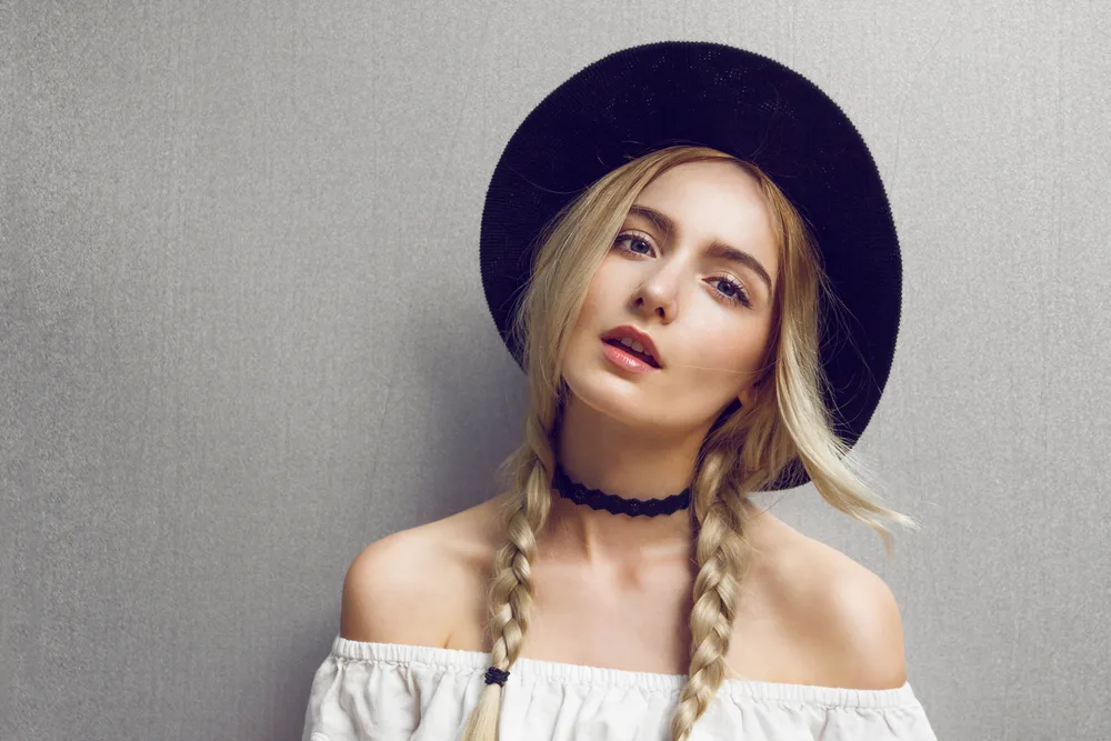 Blonde woman in hat wearing one of the top cute hairstyles for long hair with double hanging braids
