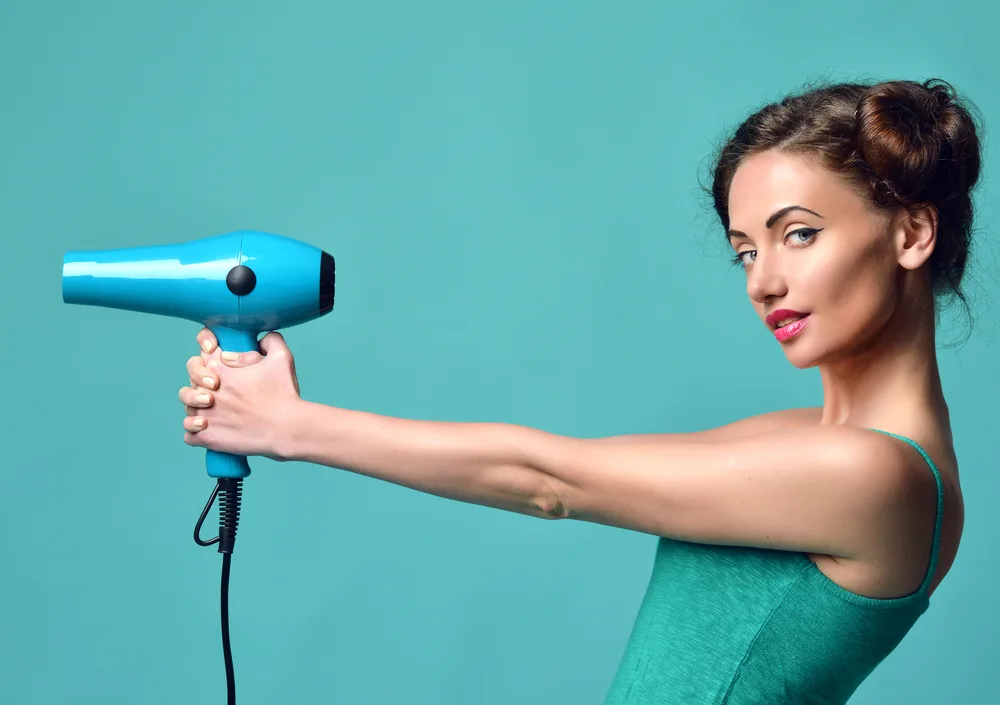 Lady holding a hair dryer like a gun while wearing a teal tank