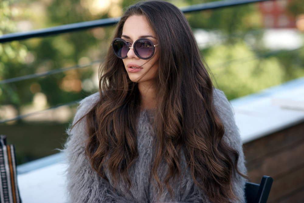 Brunette woman with dark hair has medium beach waves hair texture while wearing sunglasses and long sleeves outdoors