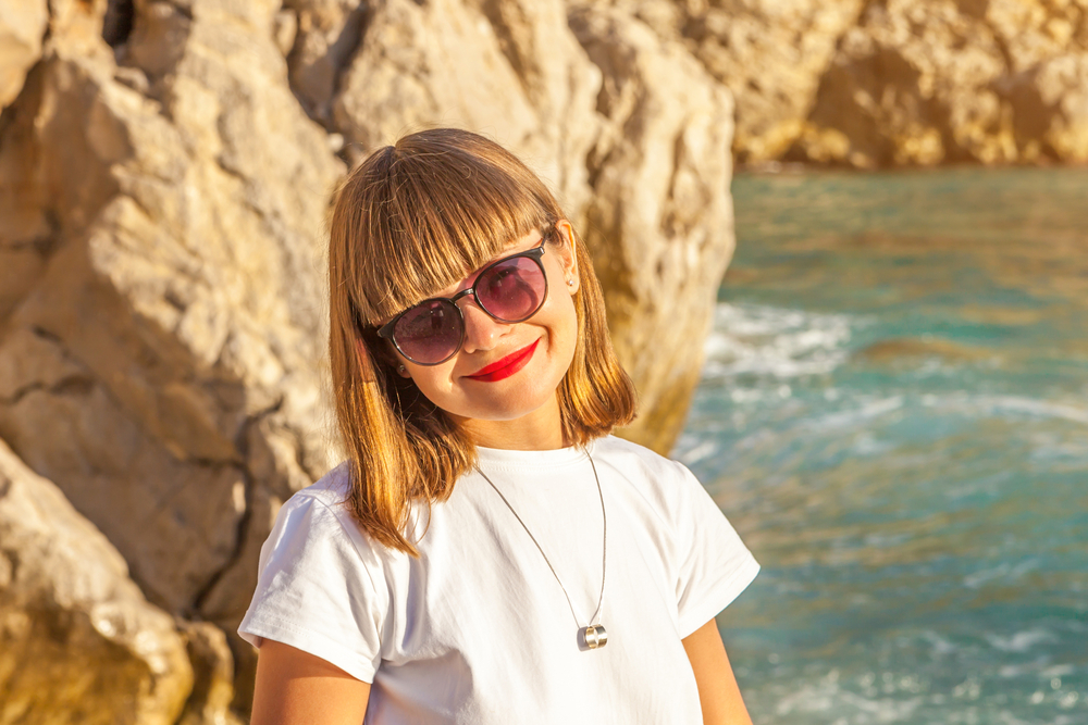 Young woman in white shirt stands on the beach at sunset with blunt bangs hairstyle and long bob